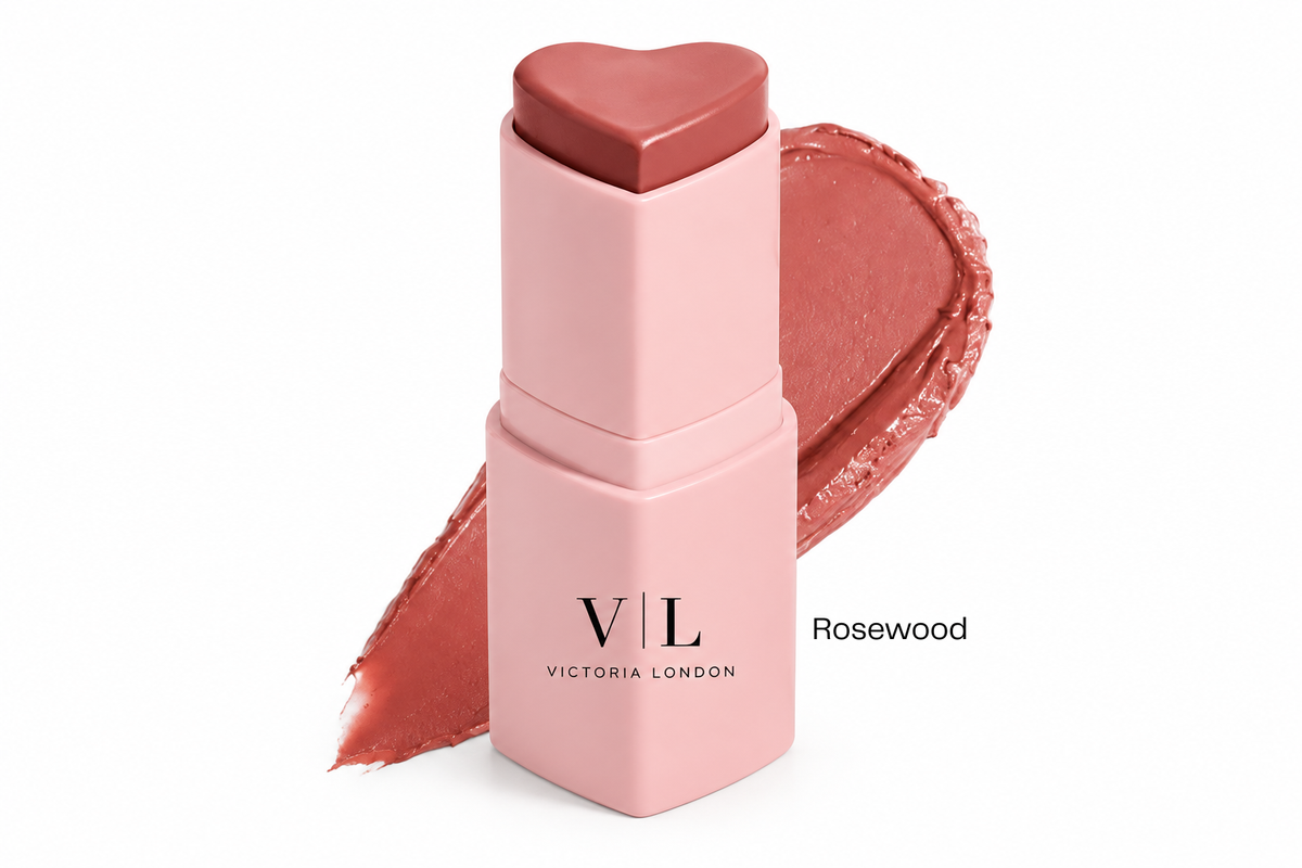Victoria London lip balm stick in the shade Rosewood, featuring a light pink square tube with a heart-shaped cap and a matching rosy brown balm bullet, shown with a textured swipe of the product on a white background.