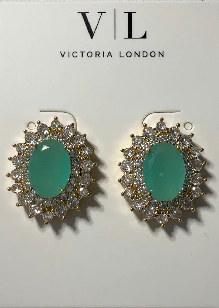 A pair of gold-plated drop earrings with oval green cabochon centers and surrounding clear cubic zirconia halos, displayed on a white Victoria London card.

Details