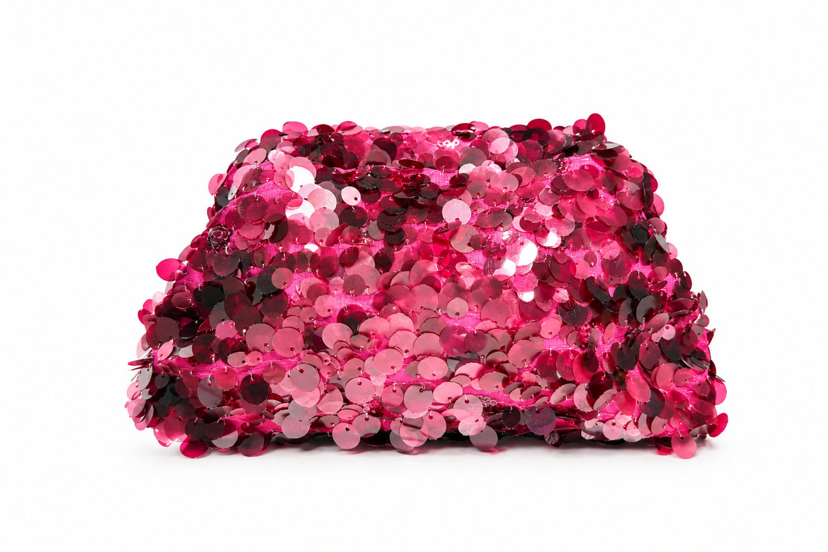 A rectangular clutch bag covered in shimmering pink and magenta sequins, resting on a white surface
